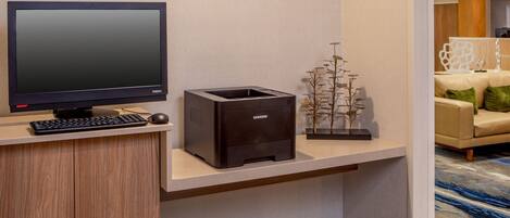 A modern office space with a flat-screen monitor, a keyboard, a printer, and a decorative plant on a shelf.