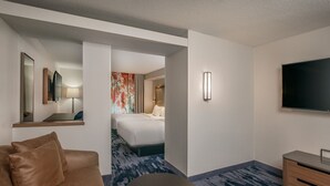 A hotel room with a sofa, a TV, a bed, a desk, and a bathroom visible through an open door. - Fairfield Inn & Suites by Marriott Brunswick Freeport (Brunswick)