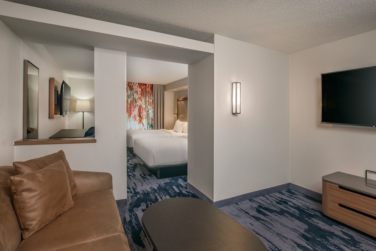 Habitación de hotel con sofá, televisión, cama, escritorio y un baño visible a través de una puerta abierta.