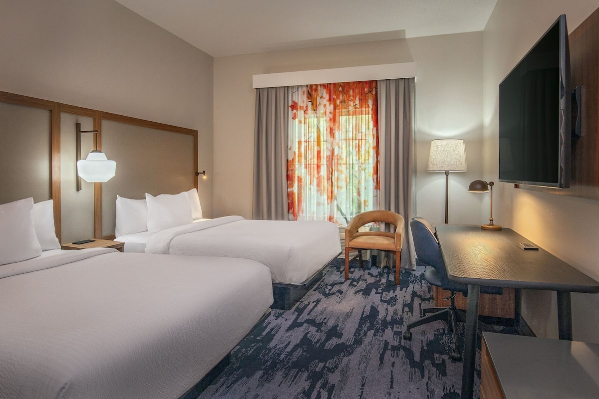 Habitación de hotel con dos camas, un escritorio, una silla, un televisor y una ventana con cortinas.