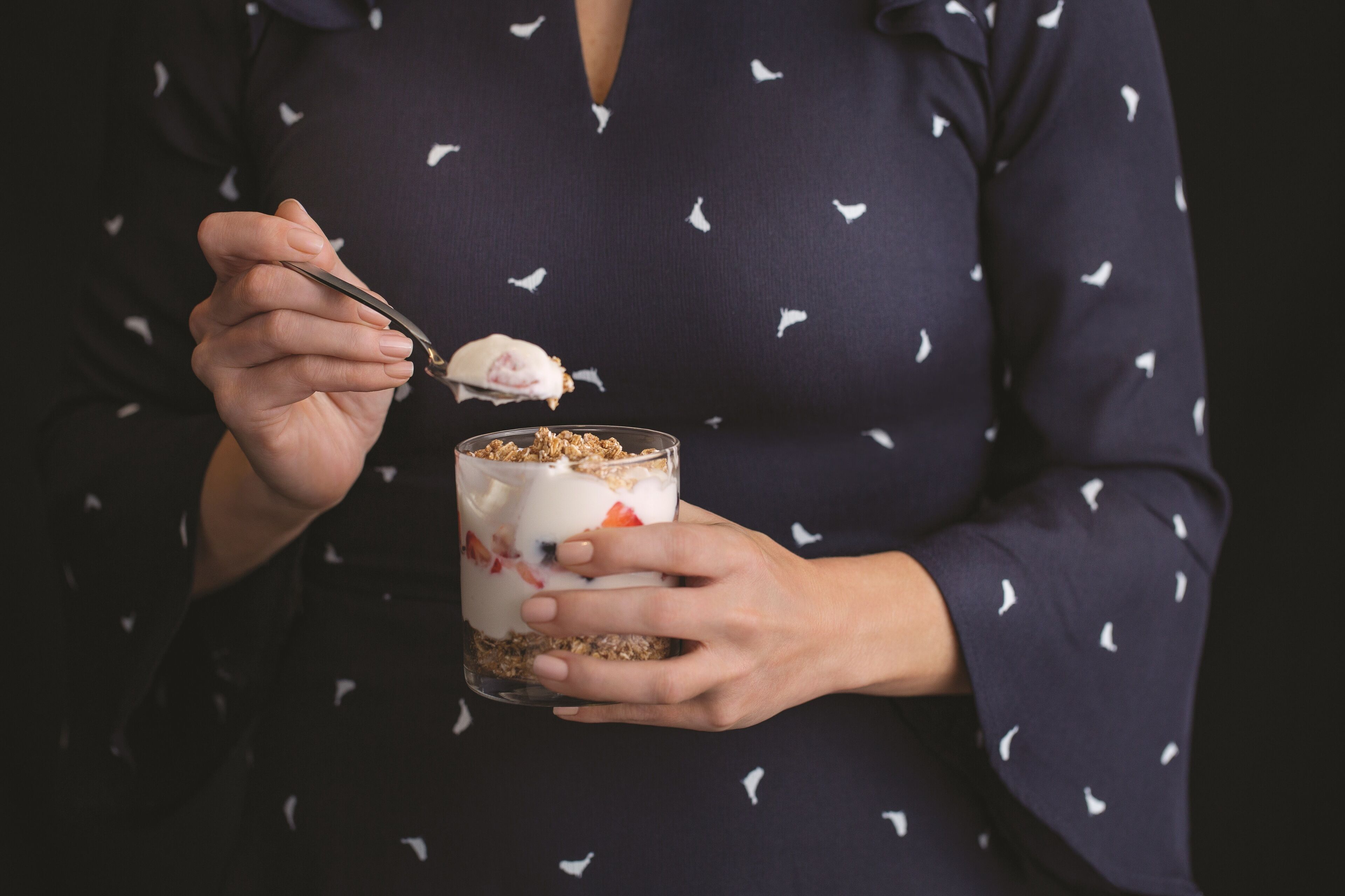 A person holding a glass of layered dessert with a spoon.