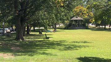 A park with a gazebo, green grass, trees, and people sitting on benches.