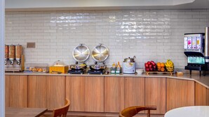 A modern kitchen with a wooden counter, two large pots, a coffee machine, and a fruit display. - Fairfield Inn & Suites by Marriott Brunswick Freeport (Brunswick)