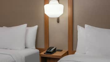 Een hotelkamer met twee bedden, een nachtkastje met een telefoon en een wandlamp.