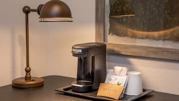 Una cafetera, una bandeja con una taza de café y una bolsa, y una lámpara sobre una mesa de madera.