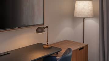 A hotel room with a wooden desk, a lamp, a chair, and a large window.