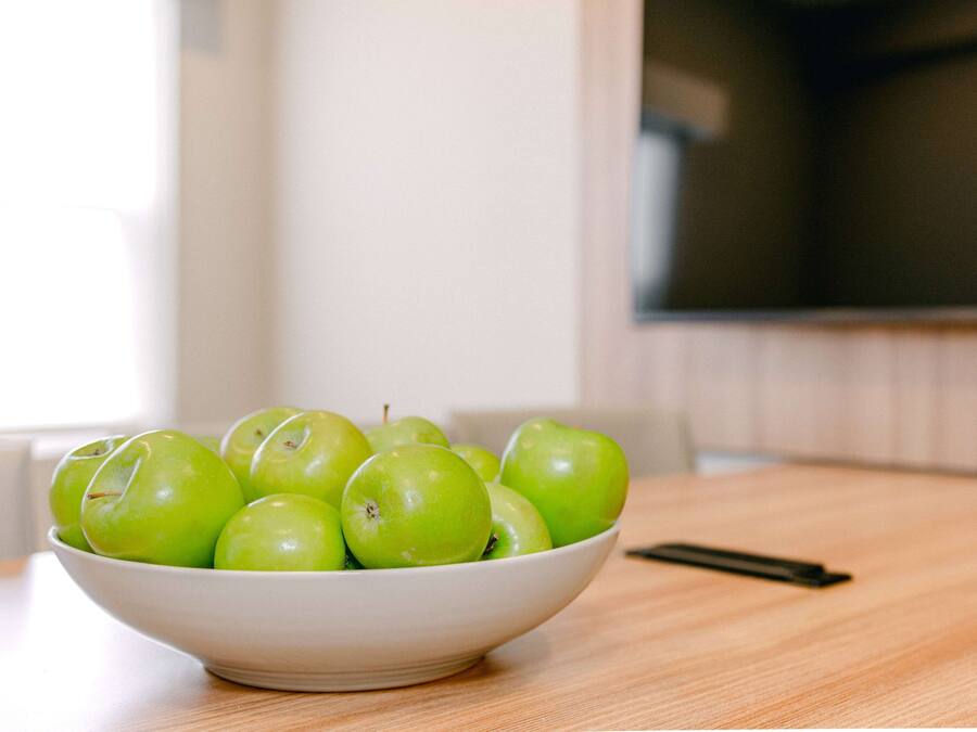 Un tazón blanco lleno de manzanas verdes sobre una mesa de madera.
