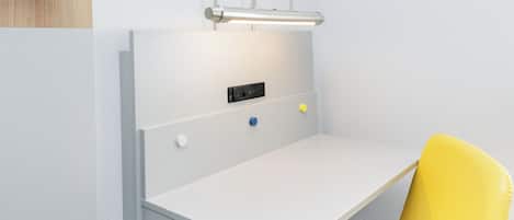 A white desk with a yellow chair, a light fixture above, and a power outlet with a blue switch.