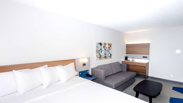 Una habitación de hotel con una cama, un sofá gris, una mesita, un escritorio con una silla y una obra de arte en la pared.