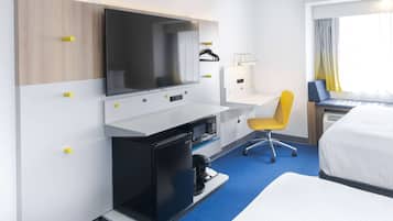 Een hotelkamer met een bed, een bureau met een computer, een televisie, een kleine koelkast en een stoel.