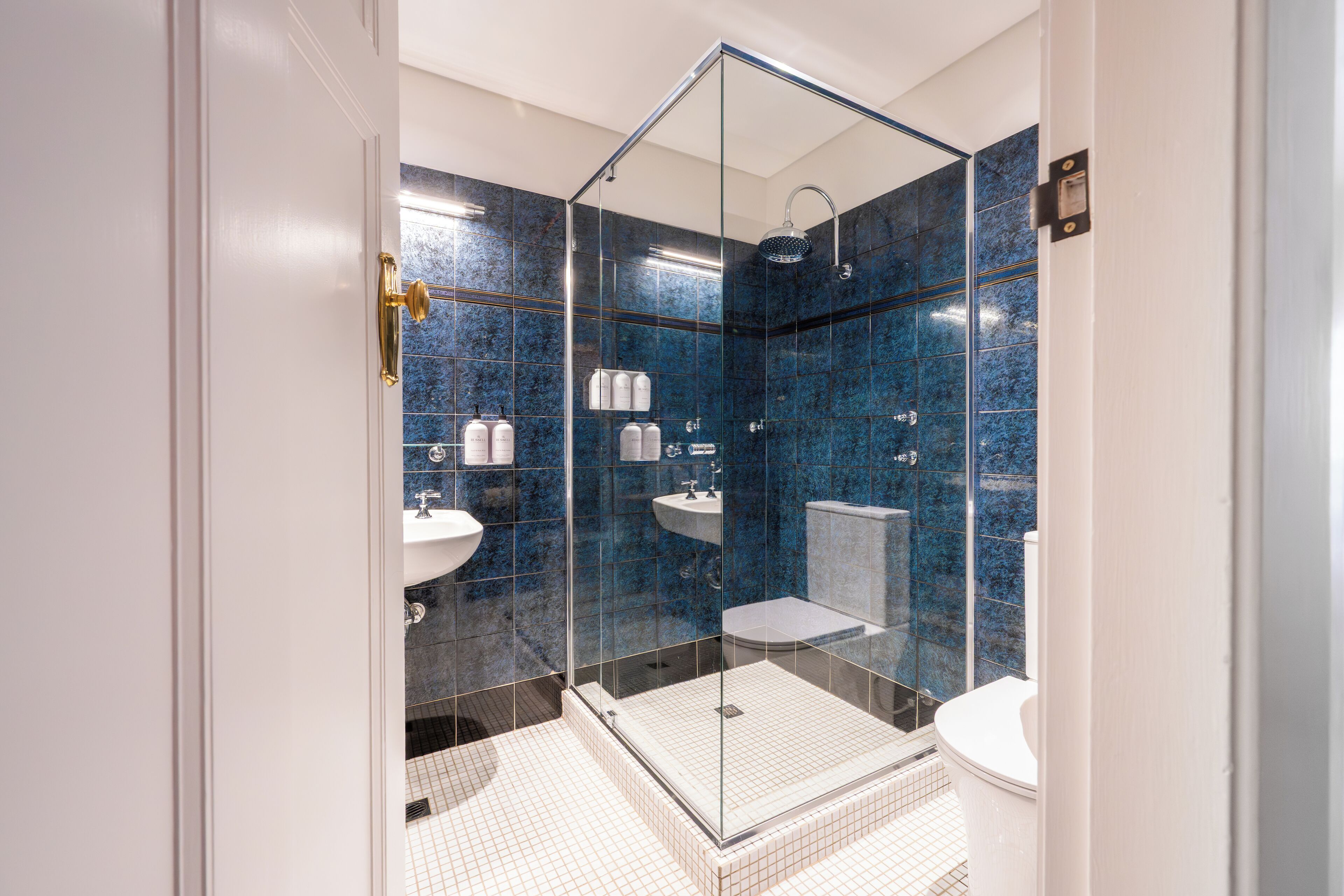Un bagno moderno con doccia vetrata, pavimento in piastrelle bianche e pareti in marmo blu.