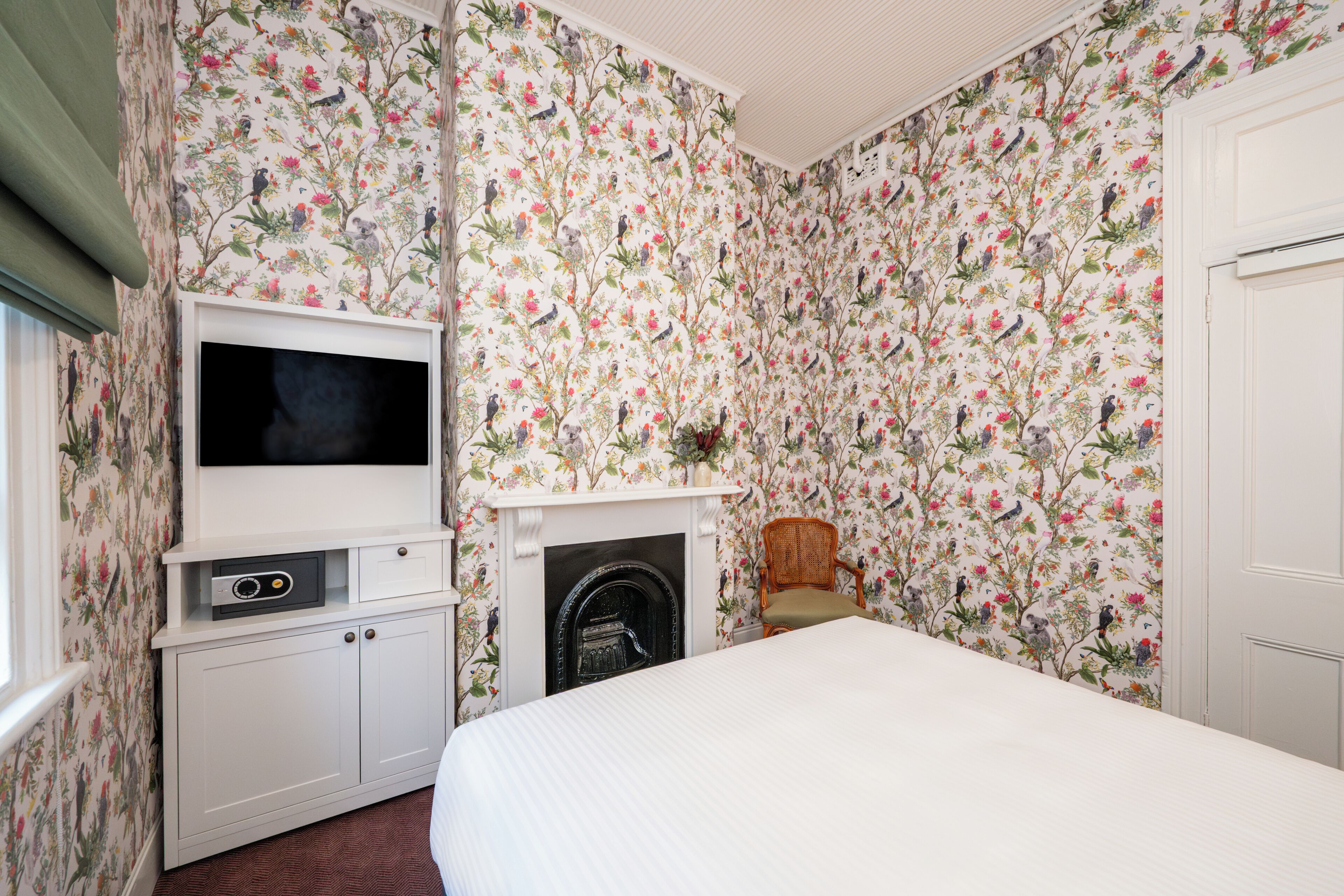 A bedroom with floral wallpaper, a television, a fireplace, and a bed.