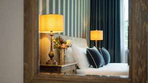 Een hotelkamer met een bed, twee bedlampjes, een nachtkastje met een lamp en een vaas met bloemen.
