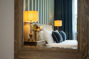 A hotel room with a bed, two bedside lamps, a nightstand with a lamp, and a vase with flowers.