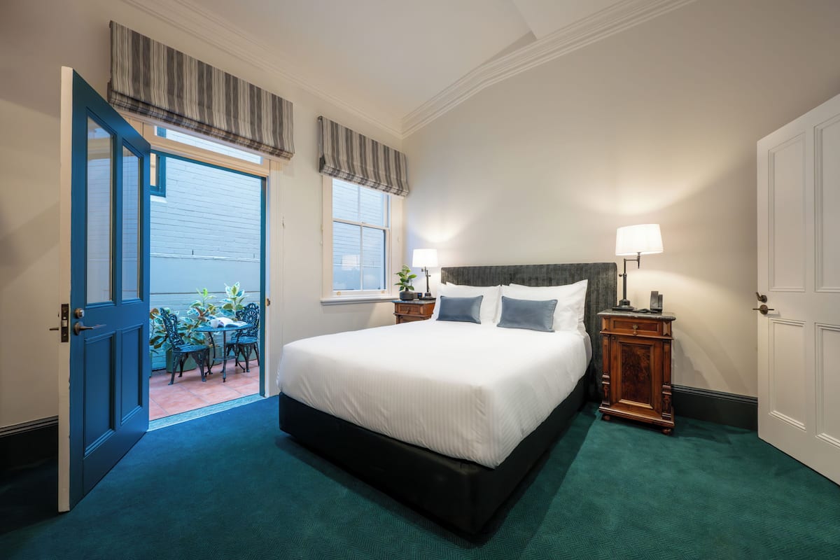 A bedroom with a large bed, a nightstand, a lamp, and a view of the outside.