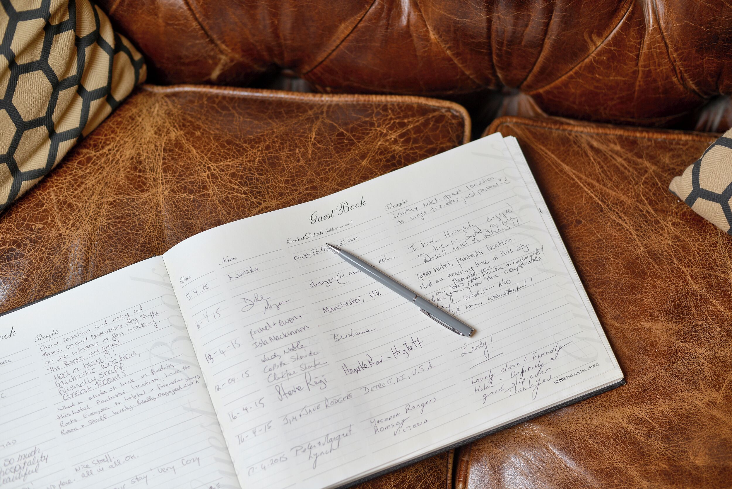 Un libro de visitas sobre un sofá de cuero marrón con anotaciones escritas a mano y un bolígrafo.