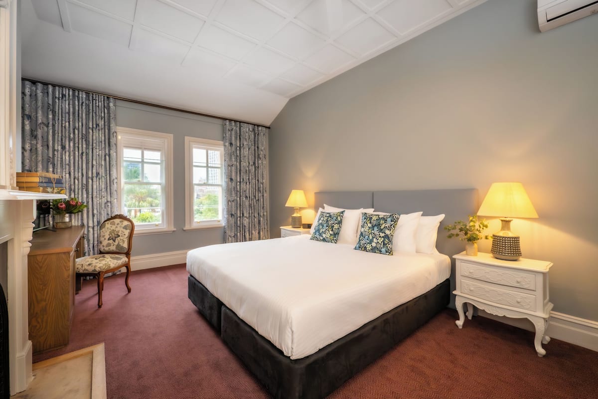 A hotel room with a large bed, two bedside tables with lamps, a chair, and a desk with a lamp.