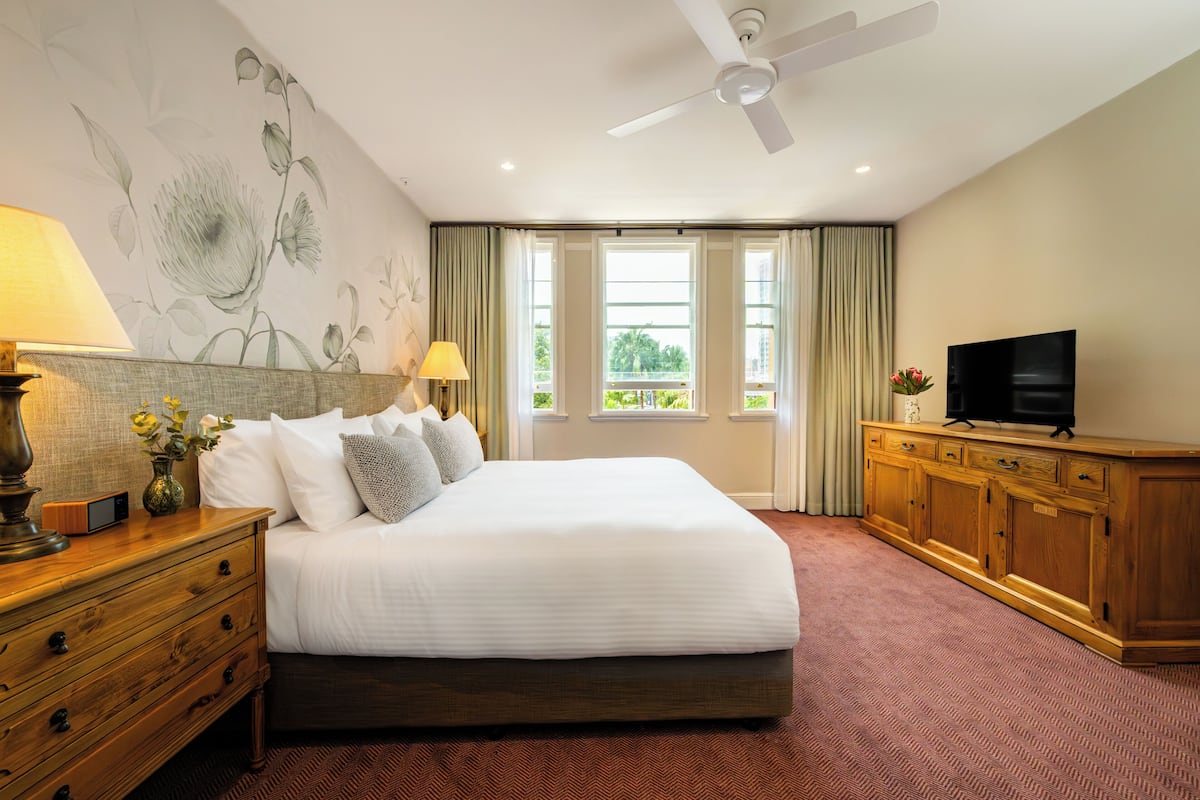A hotel room with a large bed, a wooden dresser, a flat-screen TV, and a ceiling fan.
