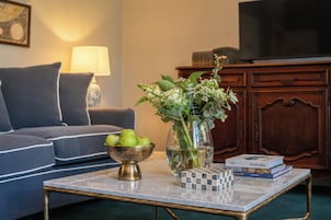 A living room with a sofa, a coffee table with a bowl of apples, a vase with flowers, and a stack of books.