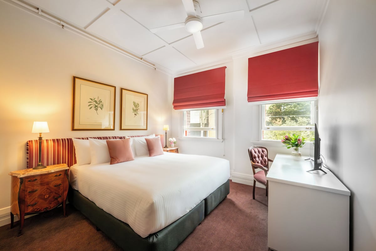 A hotel room with a large bed, a desk, a chair, a nightstand, and two framed pictures on the wall.