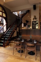 A restaurant interior with wooden flooring, a staircase, and seating arrangements.