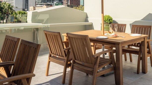 Een buitenterras met houten stoelen en een tafel, omgeven door stadsgebouwen.
