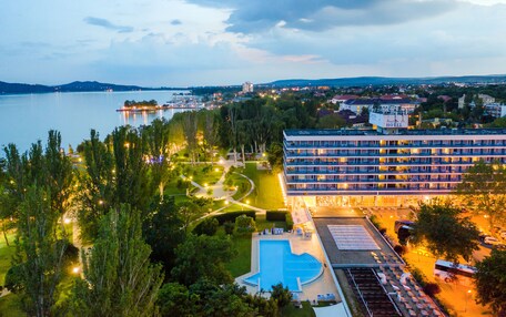 A hotel with a swimming pool, surrounded by greenery and a view of a lake.