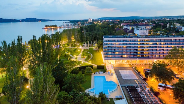A hotel with a swimming pool, surrounded by greenery and a view of a lake. - Danubius Hotel Annabella (Balatonfured)
