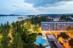A hotel with a swimming pool, surrounded by greenery and a view of a lake. - Danubius Hotel Annabella (Balatonfured)