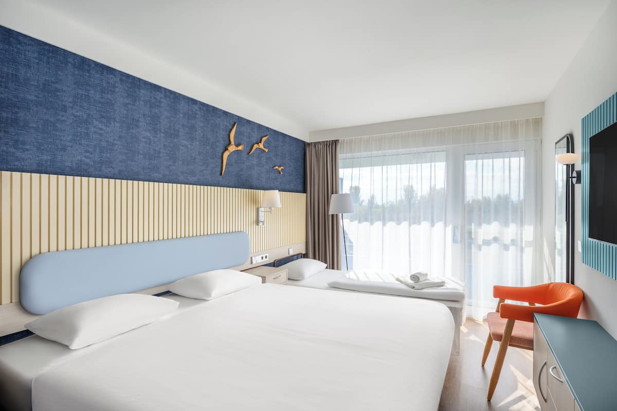 A hotel room with a large bed, a desk, a chair, a TV, and a window with curtains.
