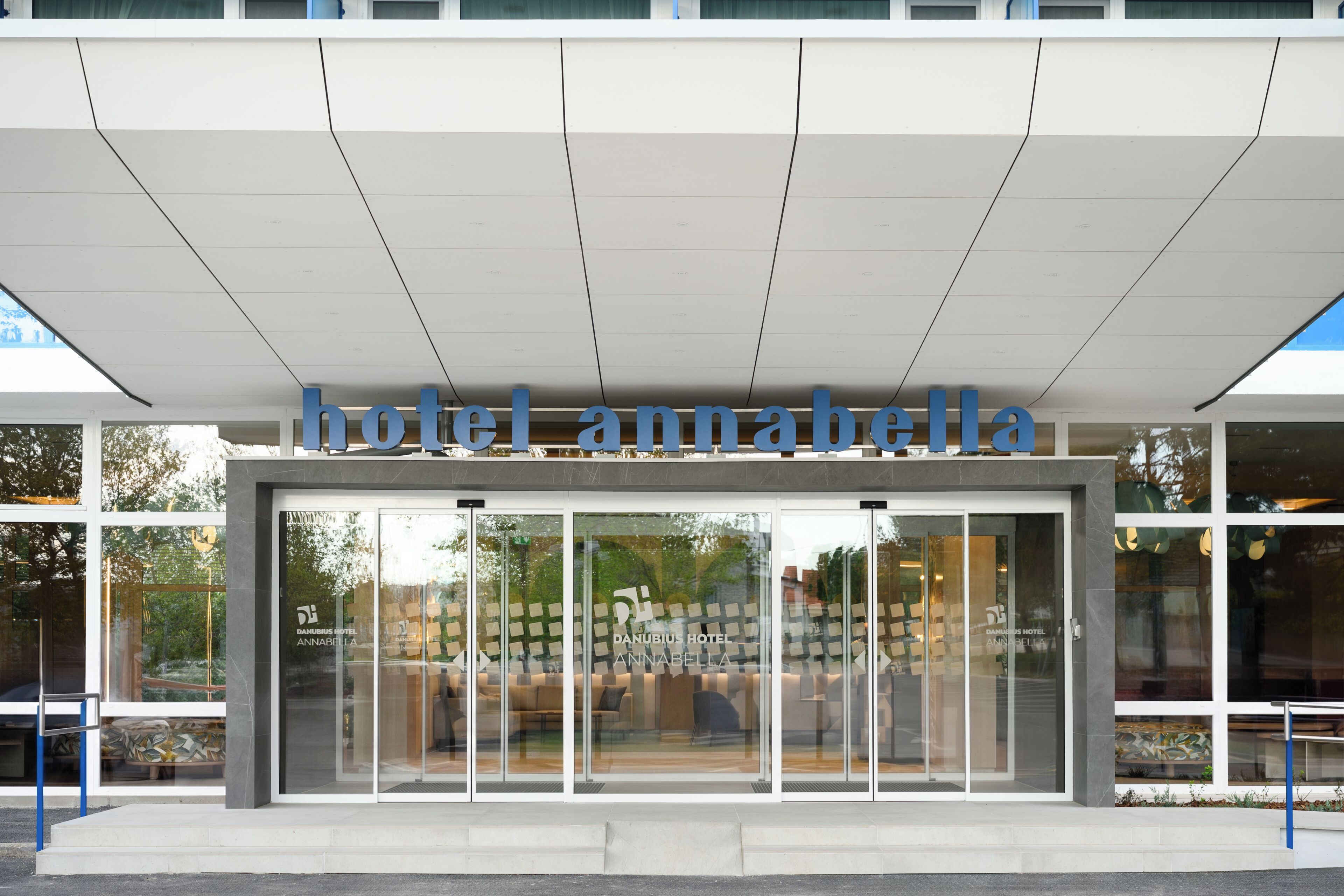 Une entrée d'hôtel moderne avec une façade en verre, une enseigne bien visible indiquant « hôtel Annabella », et un espace extérieur aménagé avec des sièges.