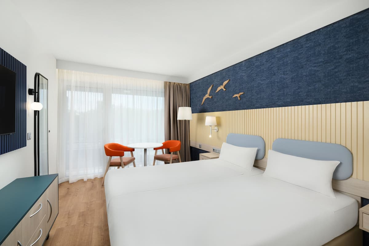 A hotel room with a large bed, a desk with two chairs, a TV, and a window with curtains.