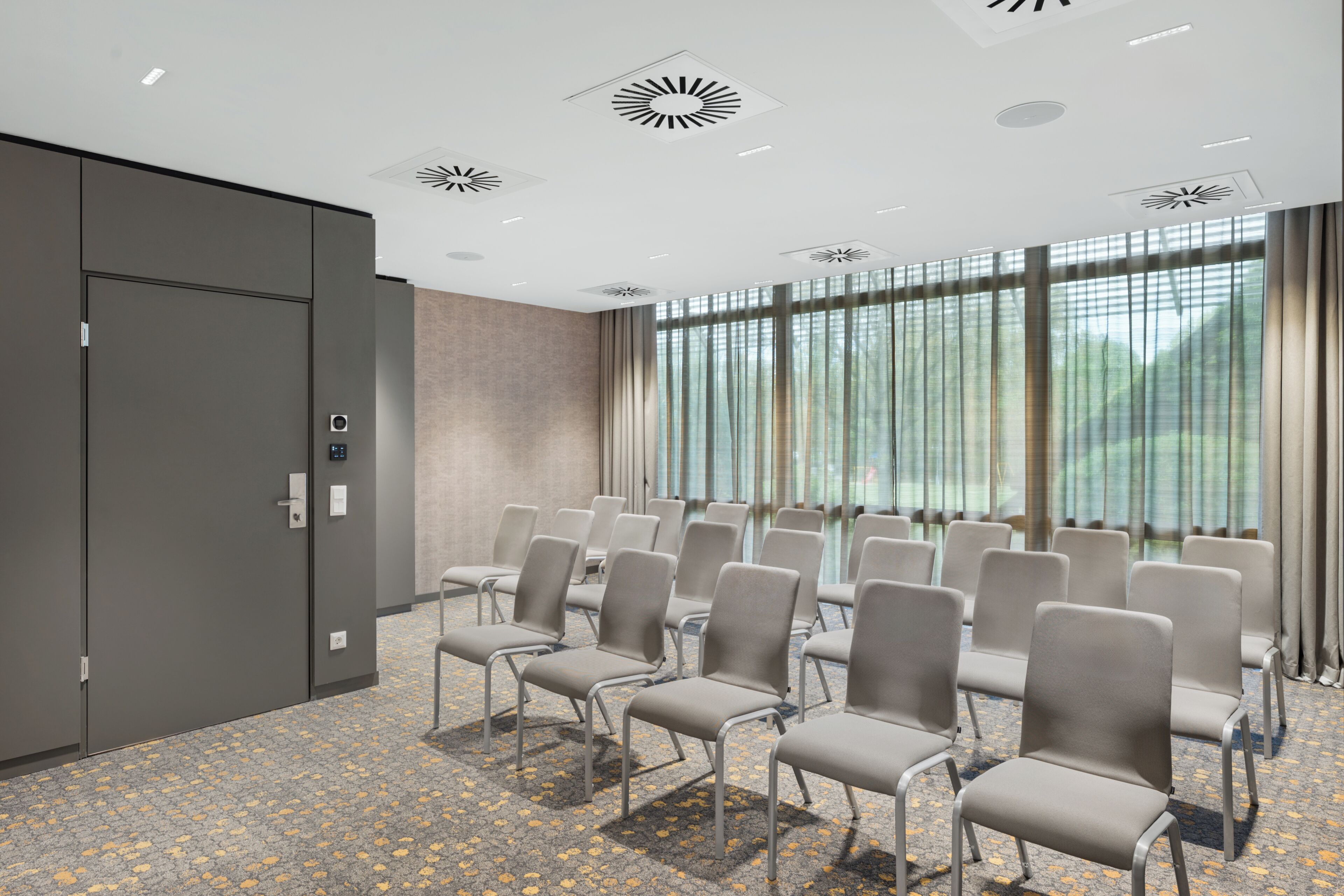 Une salle de conférence avec des rangées de chaises, une porte et une fenêtre avec des rideaux.
