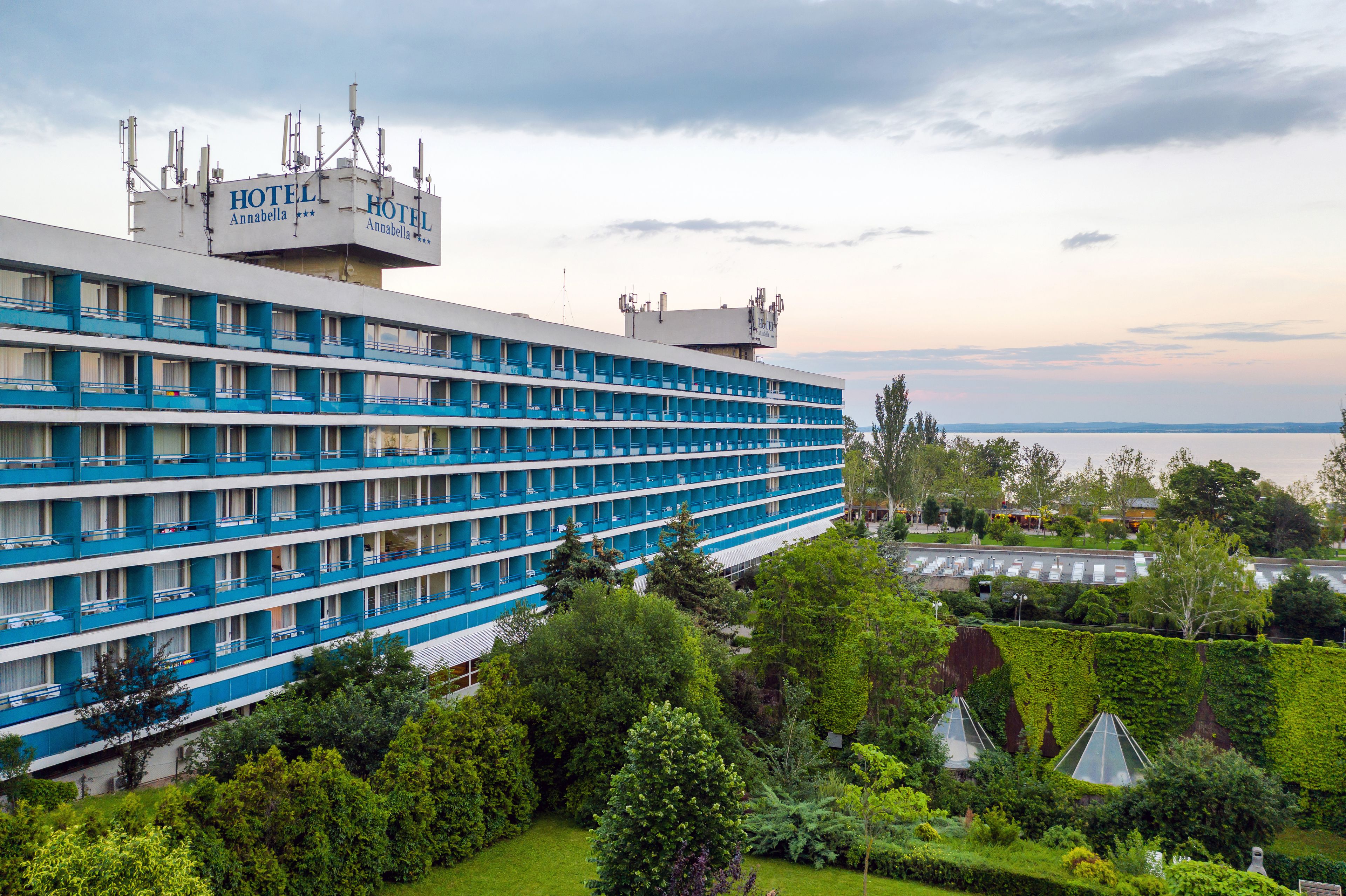 Un hotel grande con múltiples balcones, rodeado de vegetación exuberante y vistas al agua.