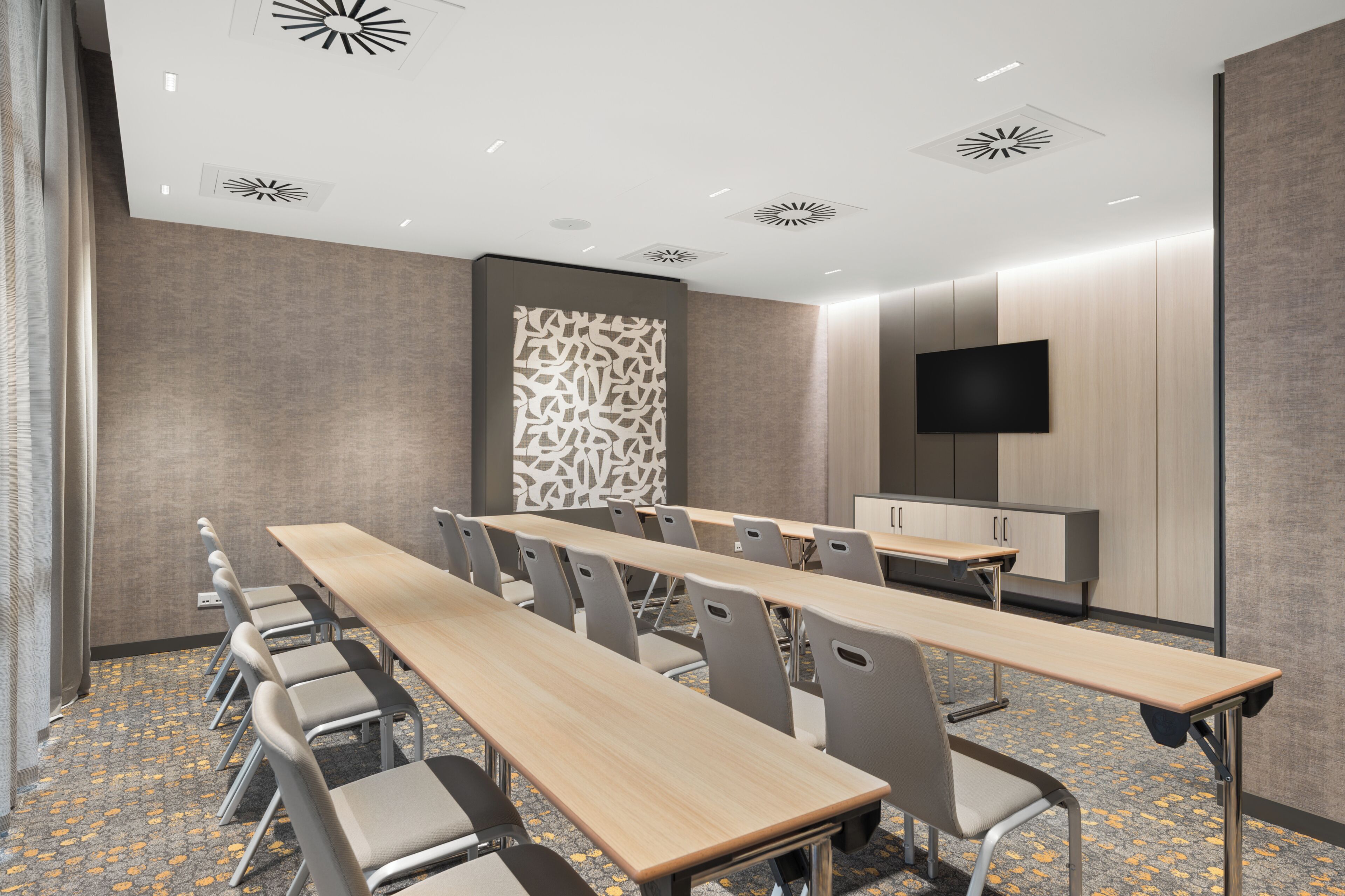 A conference room with a long table, chairs, a flat-screen TV, and a patterned wall.