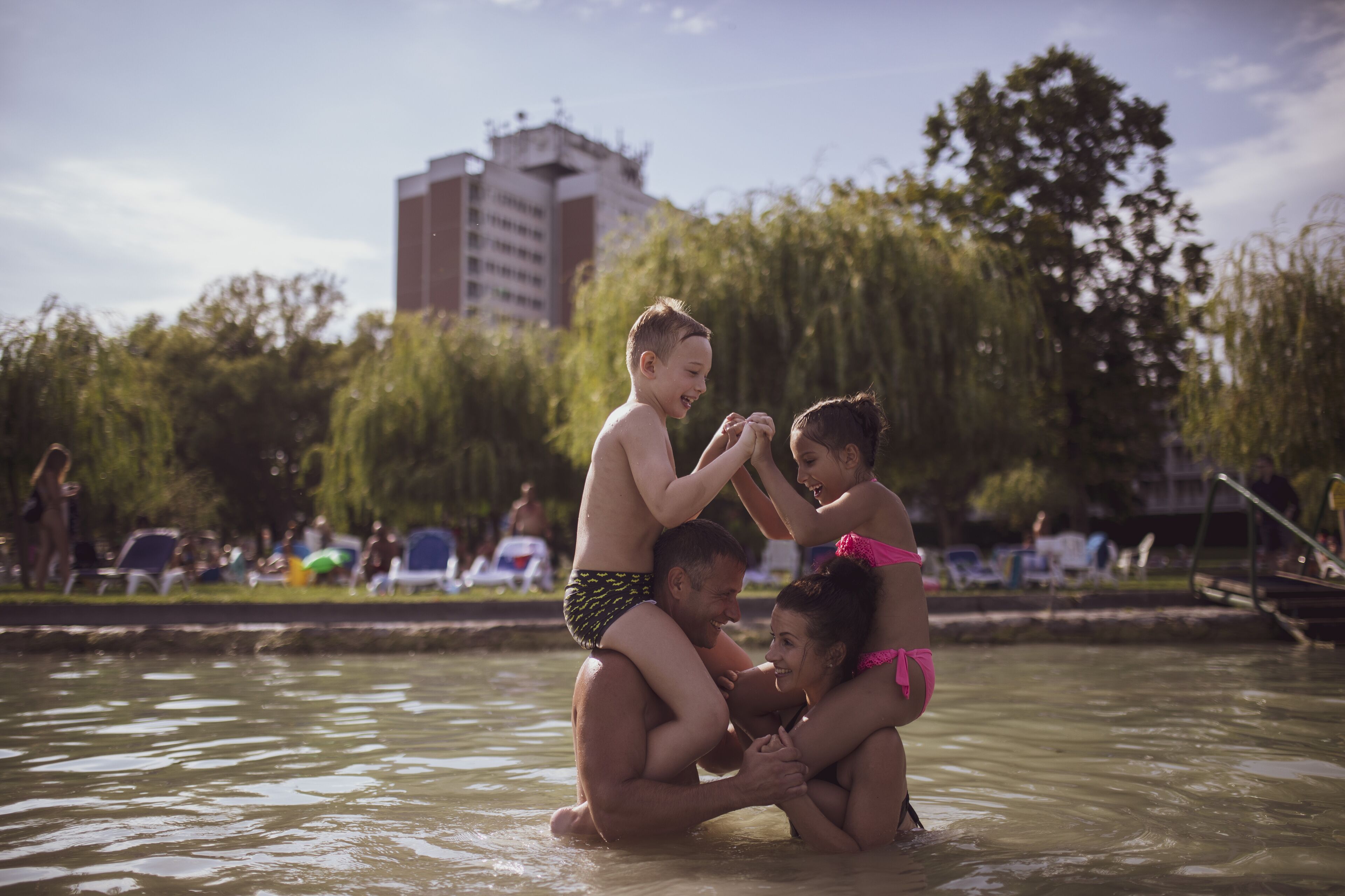 A group of people in a swimming pool with a building and trees in the background.