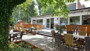 Un espace extérieur aménagé avec des chaises et des tables en osier, un bâtiment portant une enseigne indiquant «
Hôtel Danubius Marina
», et une vue sur des arbres et de la verdure.