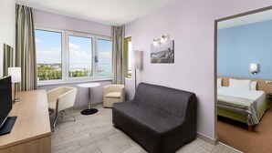Une chambre d’hôtel comprenant un lit, un canapé, un bureau avec un ordinateur, une chaise, une petite table et une fenêtre donnant sur la ville.