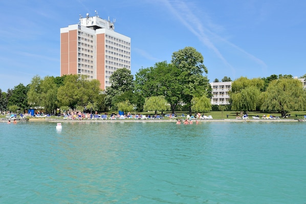 A large hotel with multiple floors, a swimming pool, and surrounding greenery.