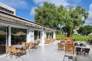 A hotel with outdoor seating and a large tree in the background. - Danubius Hotel Marina (Balatonfured)