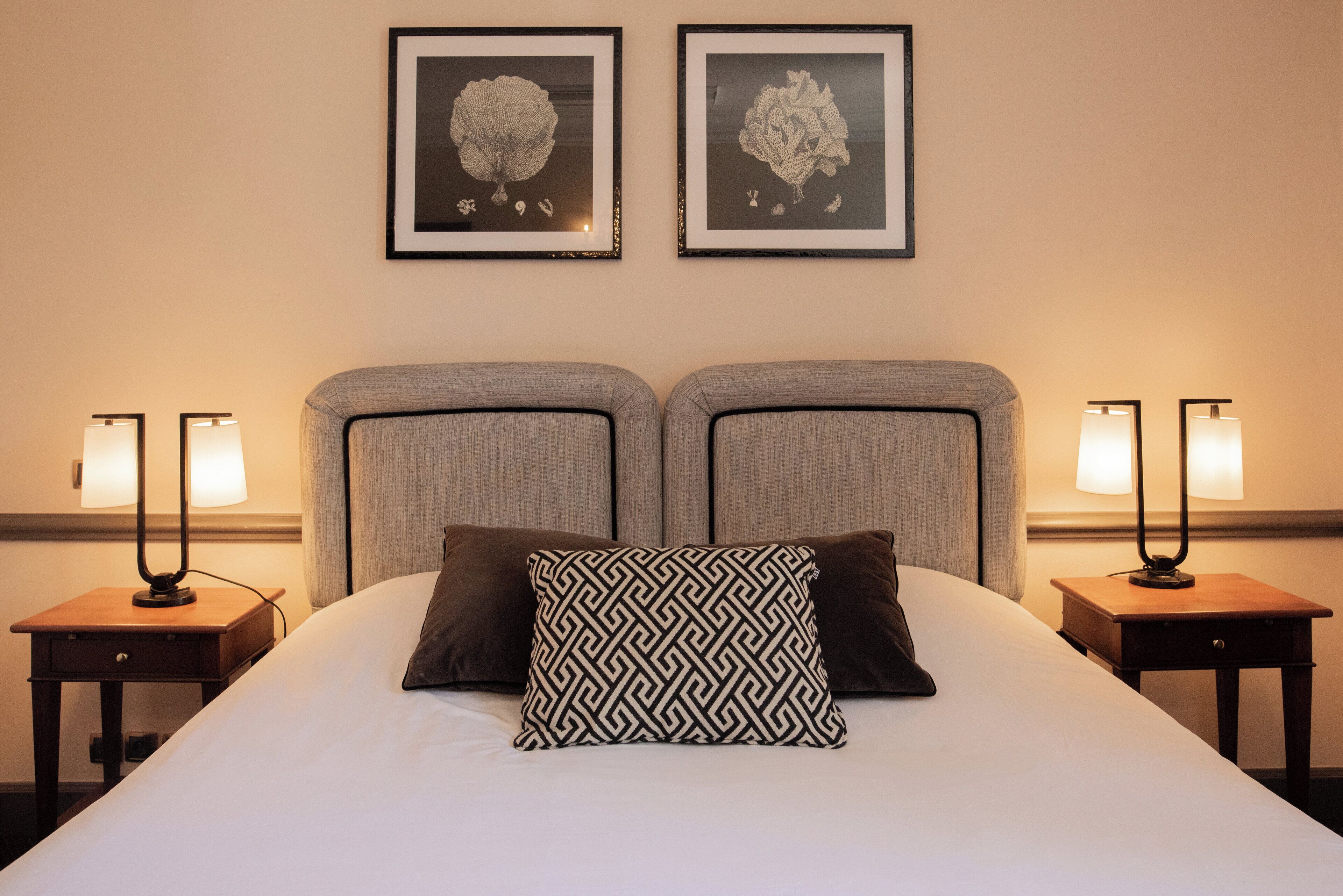 Een hotelkamer met een groot bed, twee nachtkastjes, twee wandlampen en twee ingelijste kunstwerken.