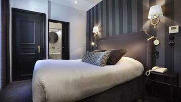 A hotel room with a large bed, a nightstand with a lamp, and a mirror on the wall.