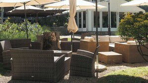 Espace extérieur aménagé avec des parasols, des meubles en osier et un bâtiment dont l’arrière-plan est constitué par une chaîne de montagnes.