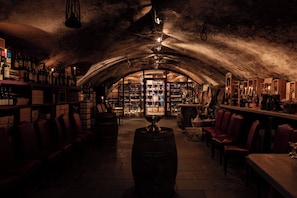 Un bar subterráneo con barriles de madera, estantes llenos de botellas y asientos de cuero.