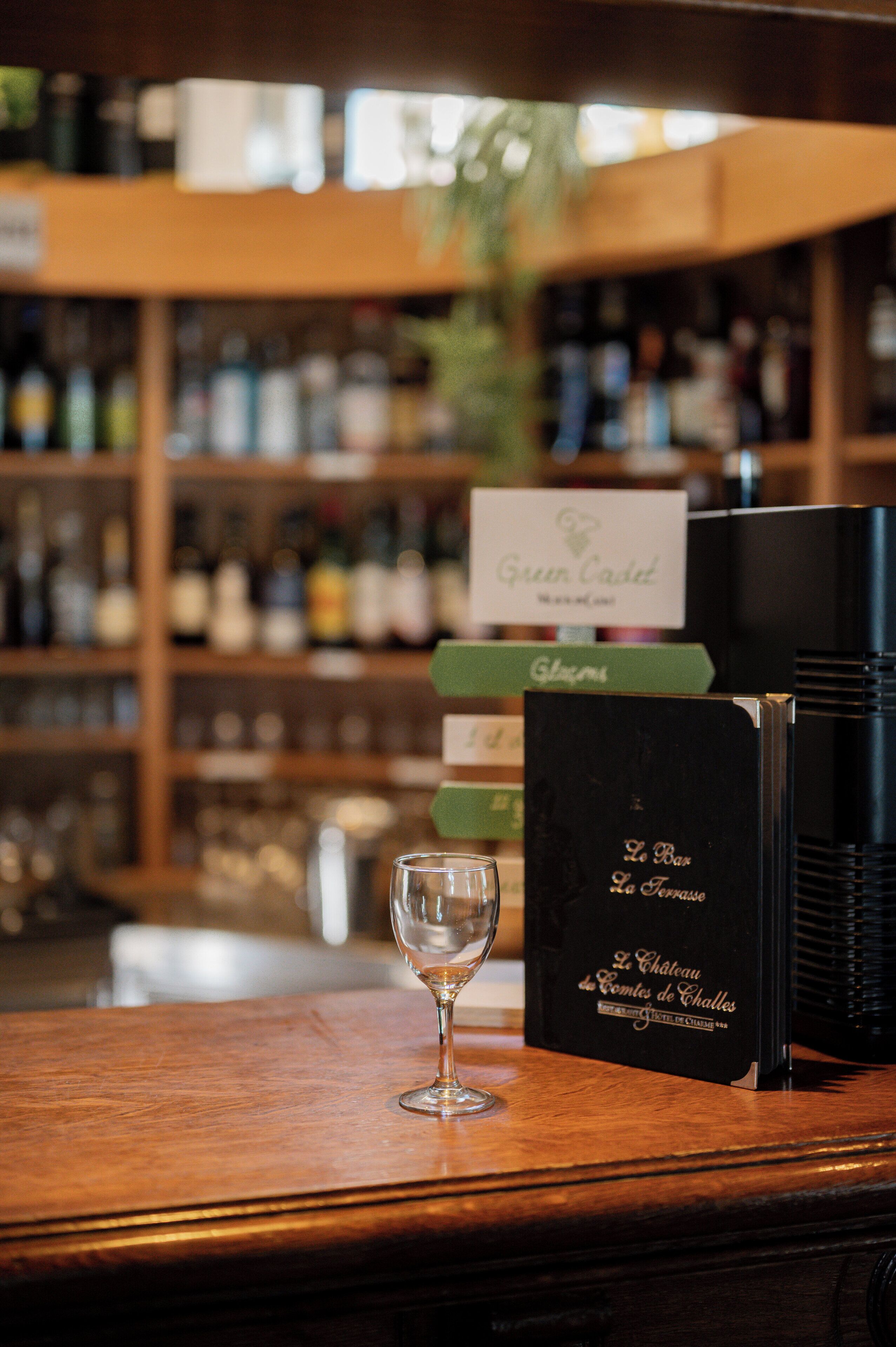 Una zona de bar con una copa de vino sobre una encimera de madera, rodeada de estantes llenos de botellas.