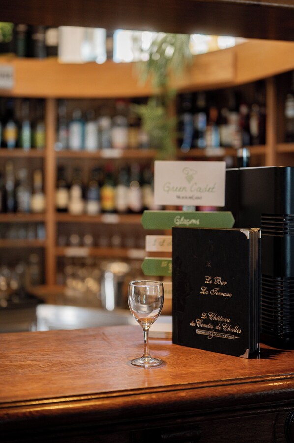 Una zona de bar con una copa de vino sobre una encimera de madera, rodeada de estantes llenos de botellas.