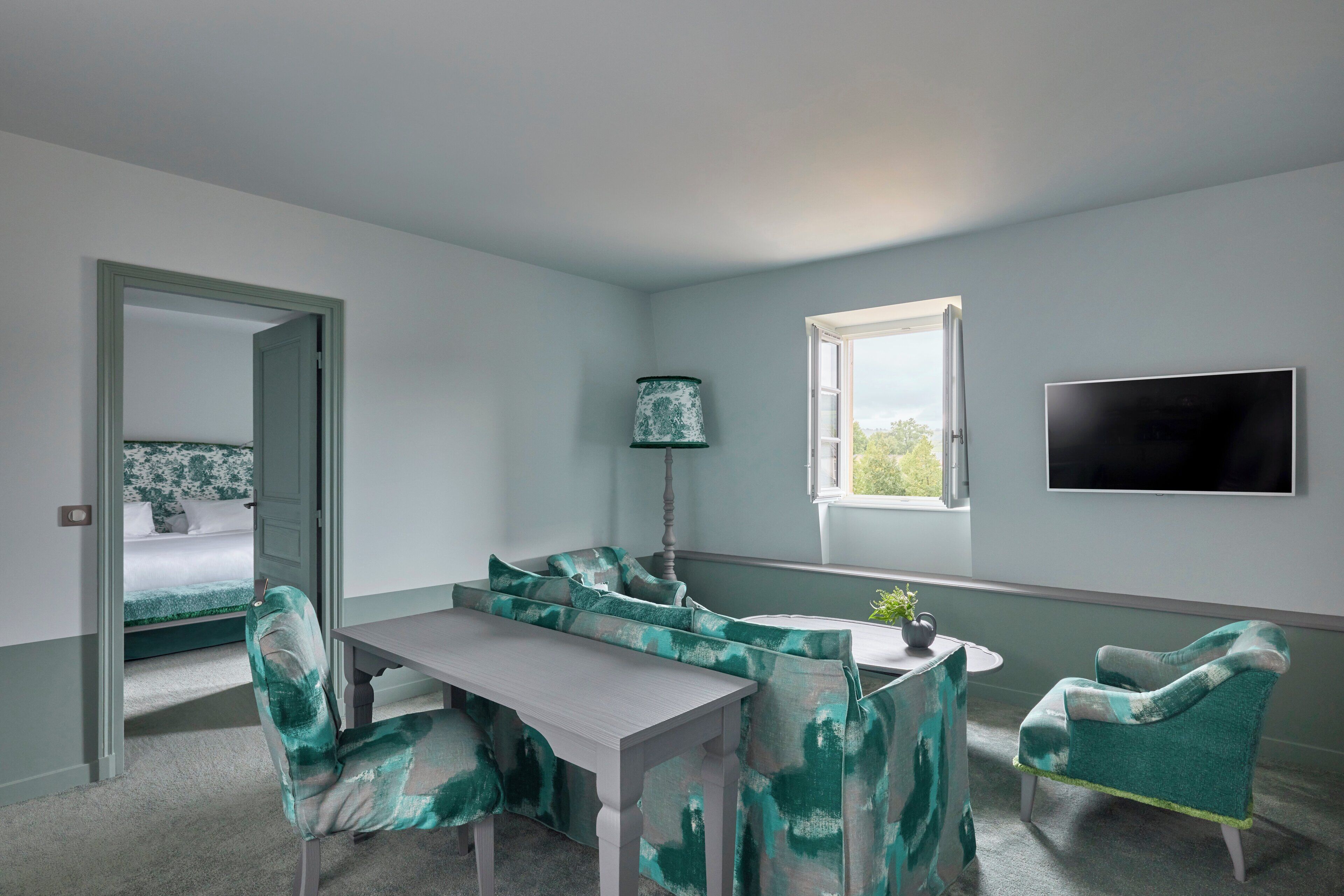 A room with a bed, a dining table, a sofa, a chair, a lamp, and a TV.