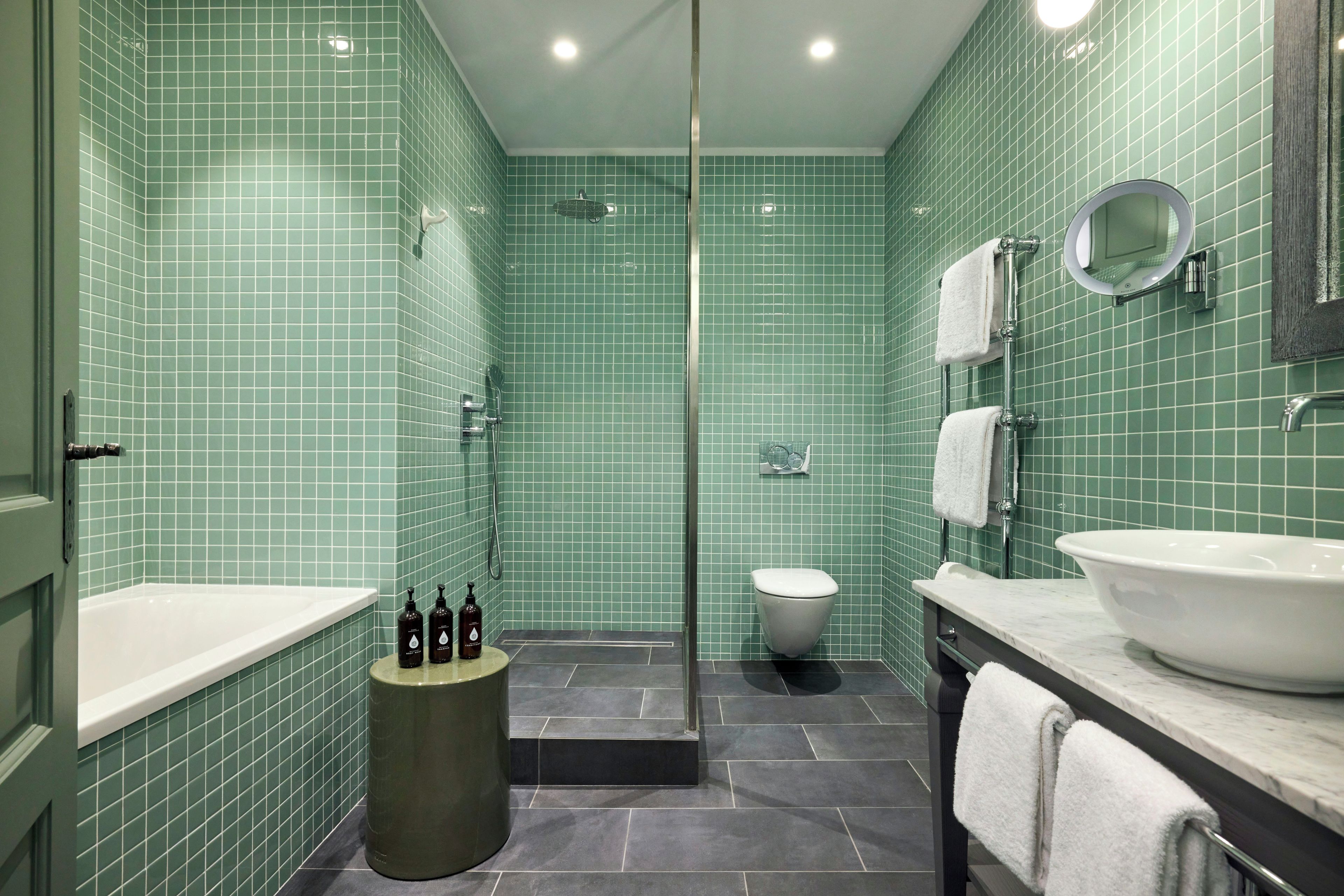 A bathroom with green tiled walls, a white toilet, a bathtub, and a sink with a mirror above it.