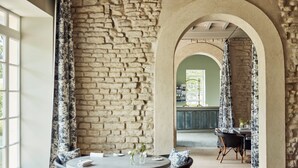 A dining area with a round table, wicker chairs, and a stone wall.