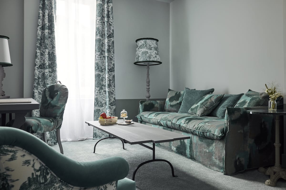 A living room with a sofa, armchairs, a coffee table, a lamp, and curtains.